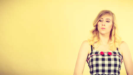 Young blonde attractive woman wearing checked top with red buttons making offended face expression being mad at someone. Studio shot on yellow backgroundの写真素材
