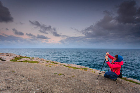 Woman photographer taking photo with camera on the most southern point of Norway in Lindesnes, South Cape, Vest-Agder, Norwayの写真素材