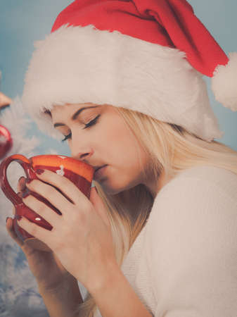 Relaxation during Christmas time concept. Woman in Santa hat holding holiday mug and drinking hot drink, coffee or tea enjoying her leisure time for relax.の写真素材