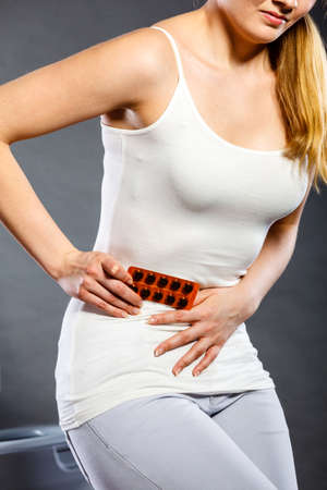 Bellyache, constipation or food poisoning. Woman suffering from strong abdominal pain, holding medical tablets activated carbon in hand, toilet in the backgroundの写真素材