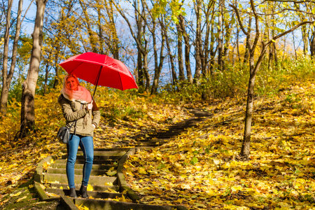 Relaxing outside concept. Woman walking in park with red umbrella, autumn bright weather.の写真素材