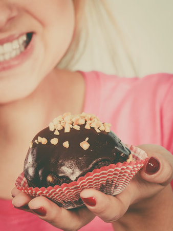 Diet, sweets, food concept. Woman holding delicious chocolate cupcake with peanut frosting about to take biteの写真素材