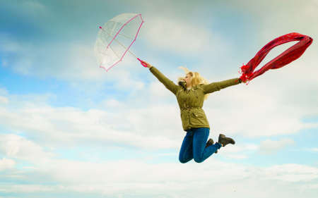 Happiness, enjoying weather, feeling great concept. Woman jumping with red scarf and transparent umbrella sky in backgroundの写真素材