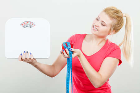 Healthy fit lifestyle, getting ready for diet concept. Happy sporty woman holding red apple, measuring tape and weight machine.の写真素材