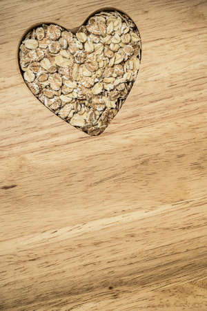 Dieting healthcare concept. Oat cereal oatmeal heart shaped on wooden surface. Healthy food for lowering cholesterol.の写真素材