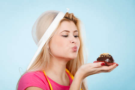 Baking tasty desserts sweets at home concept. Woman holding delicious sweet chocolate cupcake wearing apron and colander on head as hat.の写真素材