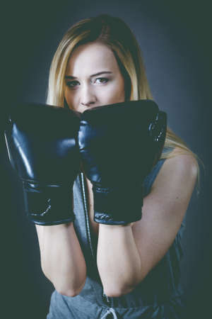 Sportsmanship fairplay and strong body. Young woman fighting boxing. Blonde girl wearing black punch gloves. Sport and fitness, power, exercising, on grayの写真素材
