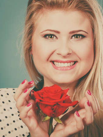 Woman holding red rose. Lovely blonde young female with flower studio shot on blue. Romance, holidays, valentine day conceptの写真素材