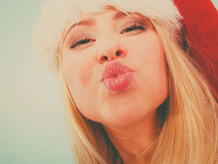 Woman wearing Santa Claus hat making funny face expressions. Christmas fun and celebration concept. Studio shot on blue background.の写真素材