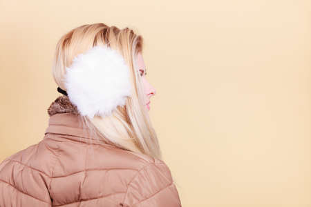 Accessories and clothes for cold days, fashion concept. Blonde woman in winter warm earmuffs and jacket, profile view.の写真素材
