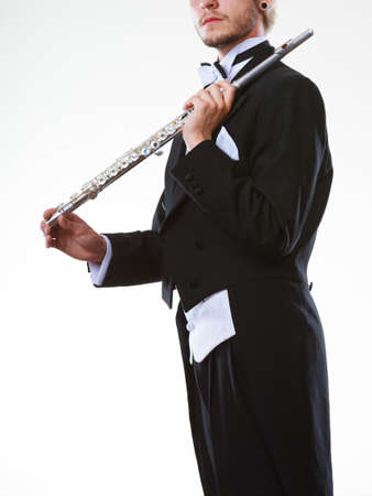 Classical music study concept. Male flutist musician performer playing flute. Young elegant man wearing tailcoat holds instrumentの写真素材