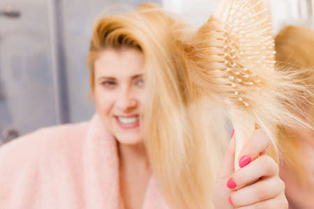 Woman wearing dressing gown brushing her long blonde hair, morning beauty routine. Haircare and hairstyling concept.の写真素材