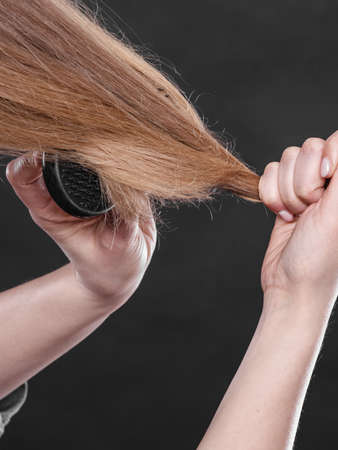 Everyday hygiene and care about good look. Back view of blonde casual girl combing her long straight hair. Woman using black comb hairbrush.の写真素材