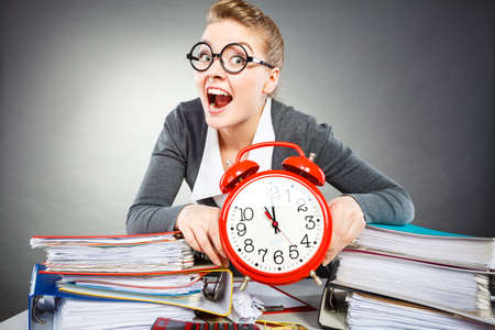 Corporate job workaholism time concept. Emotional secretary with clock. Nervous female office worker at desk with alarm ringer.の写真素材