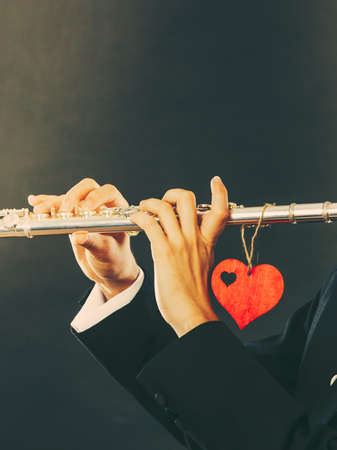 Valentines day love melody concept. Flute music playing man flutist musician performer. Male hands with instrument and red heart, close upの写真素材