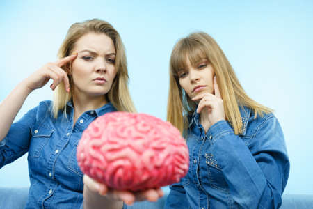 Friendship, human relations concept. Two women friends or sisters wearing jeans shirts, thinking about solving problem holding fake brain.の写真素材
