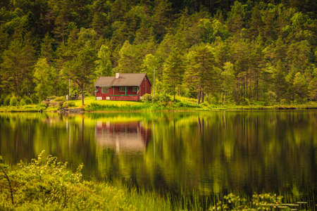 Wooden cabin hytte in norwegian green forest on water lake shore. Beautiful landscape in Norway, Scandinaviaの写真素材