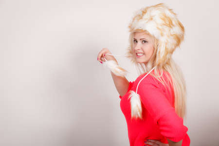 Outfit for cold days ideas, fashion and clothing concept. Attractive smiling blonde woman wearing furry winter hat holding furr tailの写真素材