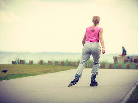 Holidays, active lifestyle freedom concept. Young fit woman on roller skates riding outdoors on sea coast, girl rollerblading on sunny dayの写真素材