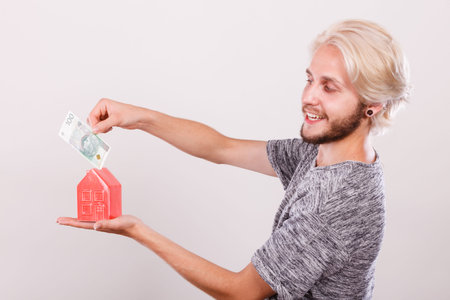 Household savings and finances, economy concept. Smiling man putting zlotych money into a piggy bank...