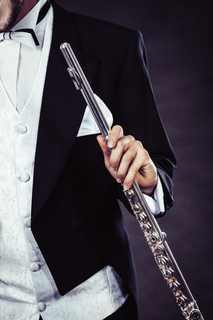 Classical music, passion and hobby concept. Elegantly dressed musician man holding flute. Studio shot on dark backgroundの写真素材