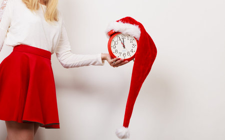 Closeup of woman holding alarm clock with santa claus hat. Christmas time season concept.
