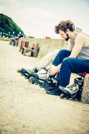 Young people friends in training suit putting on roller skates outdoor. Woman and man sitting on bench.の写真素材