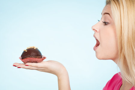 Diet, sweets, food concept. Woman holding delicious chocolate cupcake with peanut frosting about to...