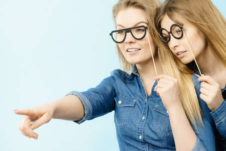 Friendship, human relations concept. Two happy women friends or sisters wearing jeans shirts pointing somewhere.の写真素材