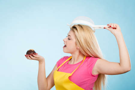 Baking tasty desserts sweets at home concept. Woman holding delicious sweet chocolate cupcake wearing apron and colander on head as hat.の写真素材
