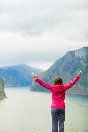 Travel concept. Happy free tourist woman in happiness and elated enjoyment with arms raised outstretched up looking at fjords mountains in Norwayの写真素材