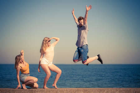 Friendship freedom summer holidays concept. Group of friends boy two girls spending time together guy  jumping against skyの写真素材