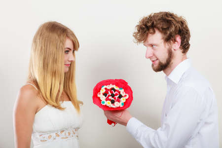 Loving couple with candy bunch bouquet flowers. Handsome man giving pretty woman present gift. Love concept.の写真素材