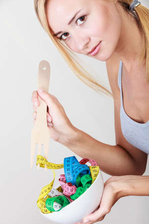 Diet, healthy eating, weight loss and slim body concept. Fit fitness girl holding bowl with many colorful measuring tapesの写真素材