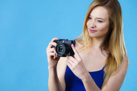 Young woman holding old fashioned analog camera taking pictures. Studio shot on blue background.の写真素材