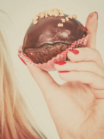 Diet, sweets, food concept. Woman hand holding delicious chocolate cupcake with peanut frosting about to take biteの写真素材