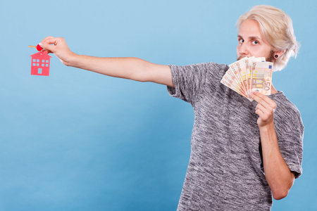 Household savings and finances, economy concept. Happy man holding money and keys to house, studio...
