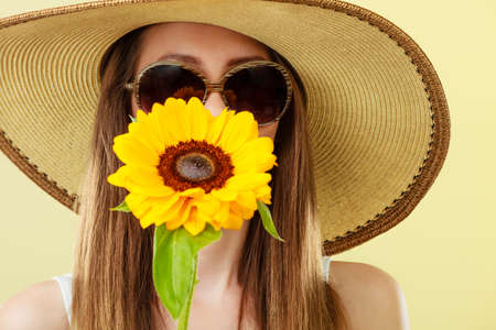 Closeup of attractive summer woman in sunglasses straw hat with sunflower in her hand on yellow backgroundの写真素材