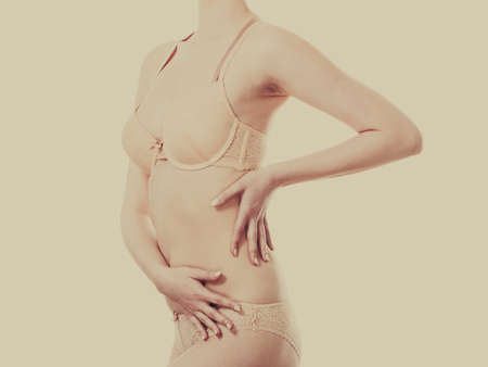 Beautiful slim healthy woman wearing lace lingerie. Attractive female showing slim sexy body in beige underwear. Studio shot toned imageの写真素材