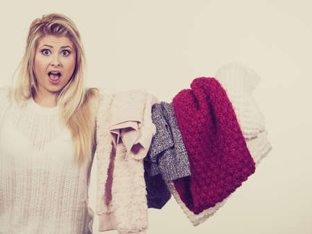 Woman holding pile of winter clothes, can not decide what to wear. Picking winter clothing concept.の写真素材