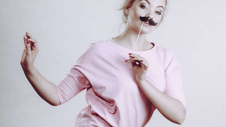 Happy woman holding fake moustache on stick having fun. Photo and carnival funny accessories concept.の写真素材