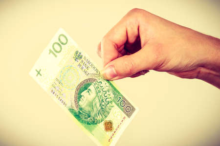 Household savings and finances, economy concept. Man putting zlotych money into a piggy bank in the shape of a house, studio shot on grey backgroundの写真素材