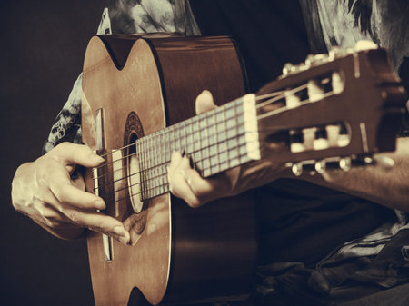 Music, sound, passion concept. Man playing on acoustic guitar, studio shot, black background, sepia...
