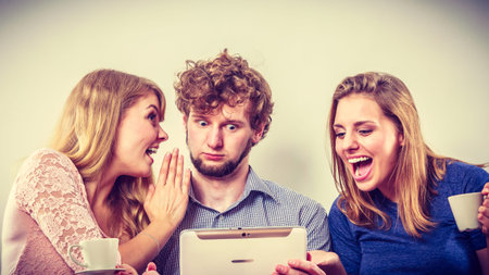 Friends browsing surfing internet on tablet. Young people man and women relaxing at home. Girl whispering to guy ear.の写真素材