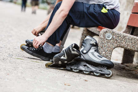 Closeup of people friends putting on roller skates outdoor. Woman and man sitting on bench.の写真素材