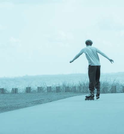 Activity, exercises content. Man rollerblading through promenade next to seaside wearing sporty clothes, back view blue colorの写真素材