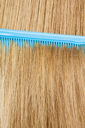 Combing and brushing concept. Routine everyday hygiene. Close up of detail blue comb in blonde smoothy healthy female hair.の写真素材