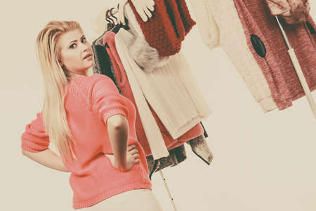 Young woman in wardrobe home closet, teen blonde girl choosing her warm fashion outfit on clothing rack. Picking winter autumn clothes, shopping concept. Toned imageの写真素材