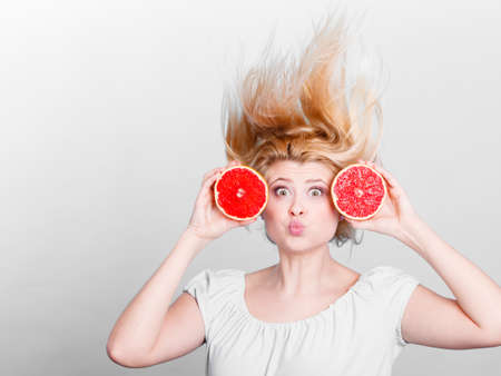 Healthy diet, refreshing food full of vitamins. Happy crazy woman holding sweet delicious citrus fruit, red grapefruit having windblown hair.の写真素材