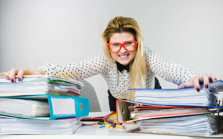 Focused business woman feeling energetic sitting working at desk full off documents in binders.の写真素材